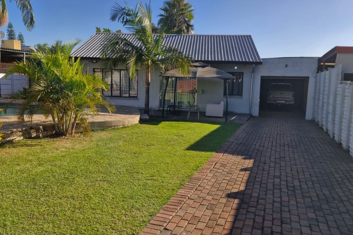Rear view of the property featuring a paved driveway, attached garage, swimming pool, and a well-maintained lawn area.