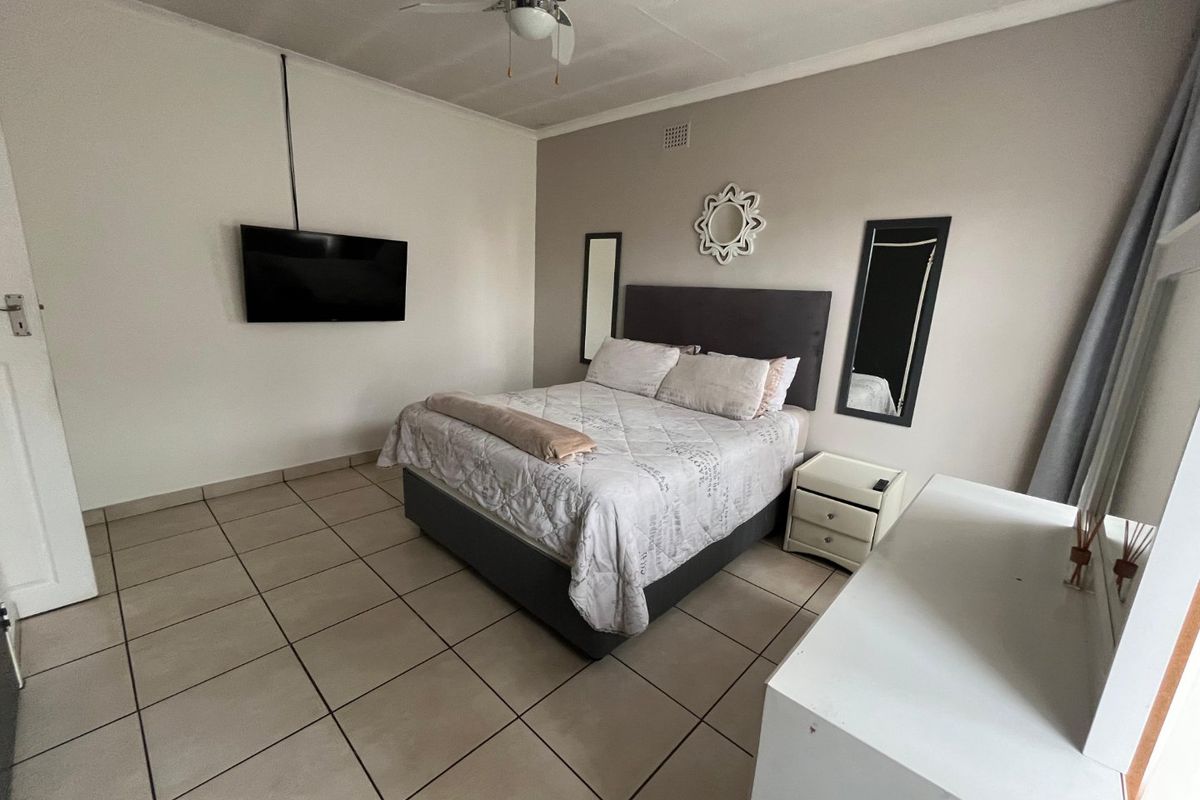 A functional bedroom featuring neutral wall tones, tiled flooring, and a ceiling fan, providing a clean and simple living space.