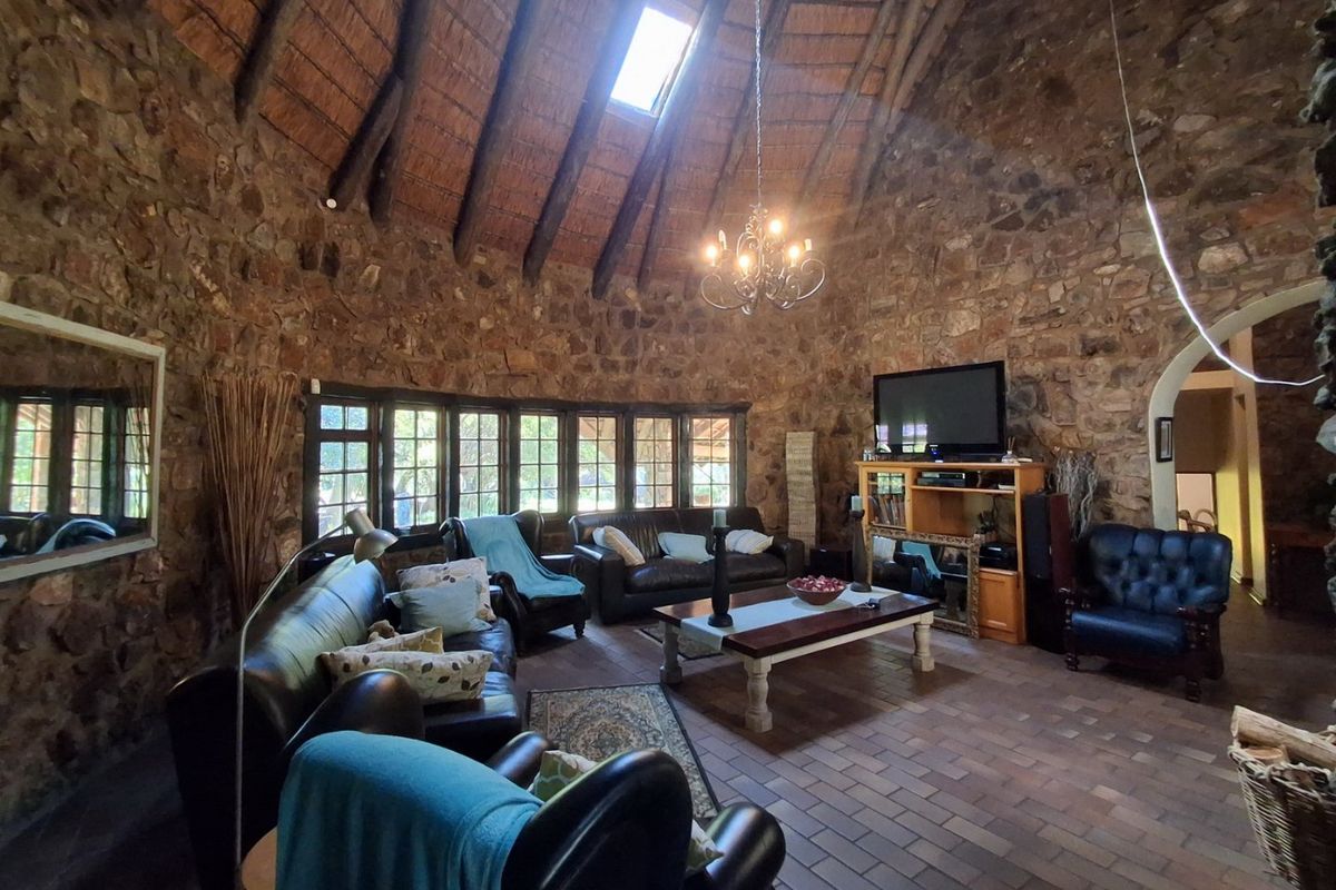 Spacious living room featuring rustic exposed stone walls, a high thatched ceiling with a skylight, and traditional brick flooring.