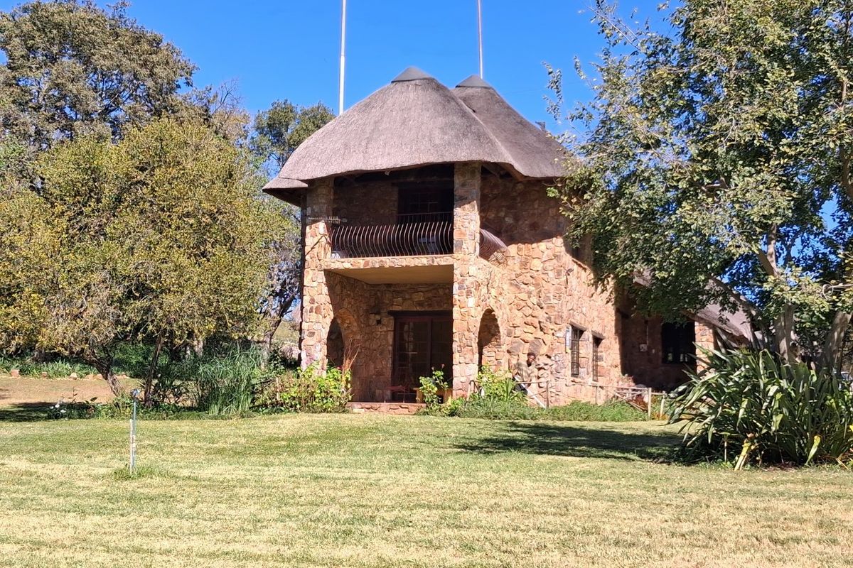 A two-story stone farmhouse featuring a traditional thatched roof, a private balcony with metal railing, and arched architectural details set within a landscaped garden.