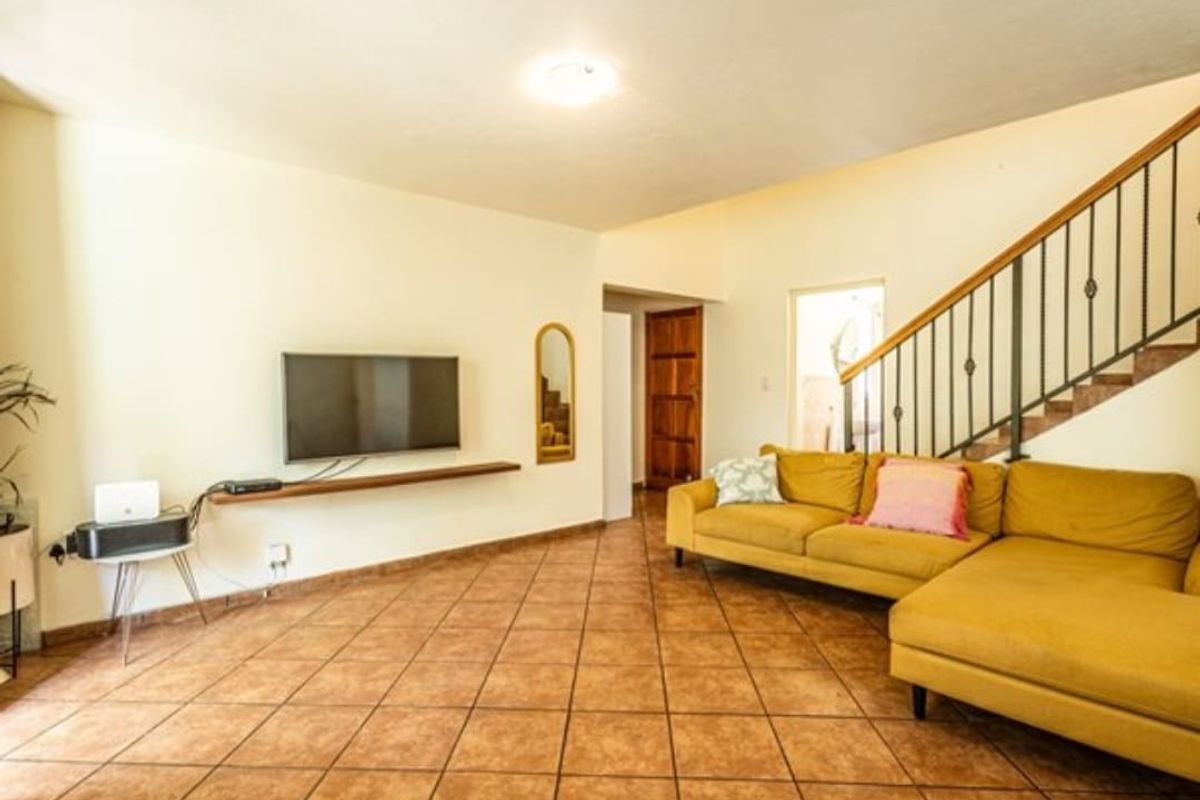 Spacious living room featuring tiled flooring, a floating media shelf, and a staircase with a decorative wrought iron balustrade.