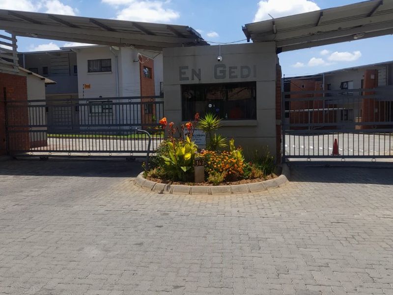 The main entrance to the En Gedi apartment complex, featuring a secure gated access point, guard house, and paved driveway.