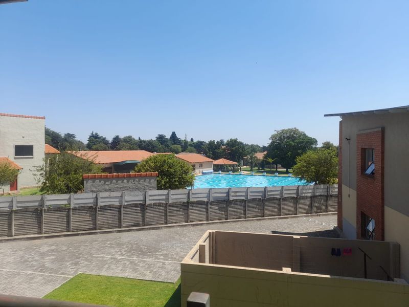 An elevated view overlooking a communal swimming pool, paved driveway, and landscaped grounds within the apartment complex.