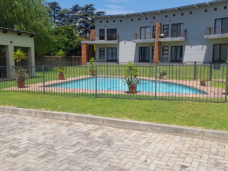 A well-maintained communal swimming pool area featuring secure metal fencing, paved surrounds, and views of the apartment building facade.