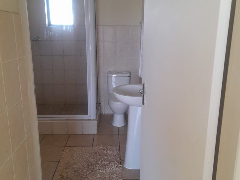 A functional bathroom featuring a shower enclosure, pedestal basin, and toilet with neutral ceramic floor and wall tiling.