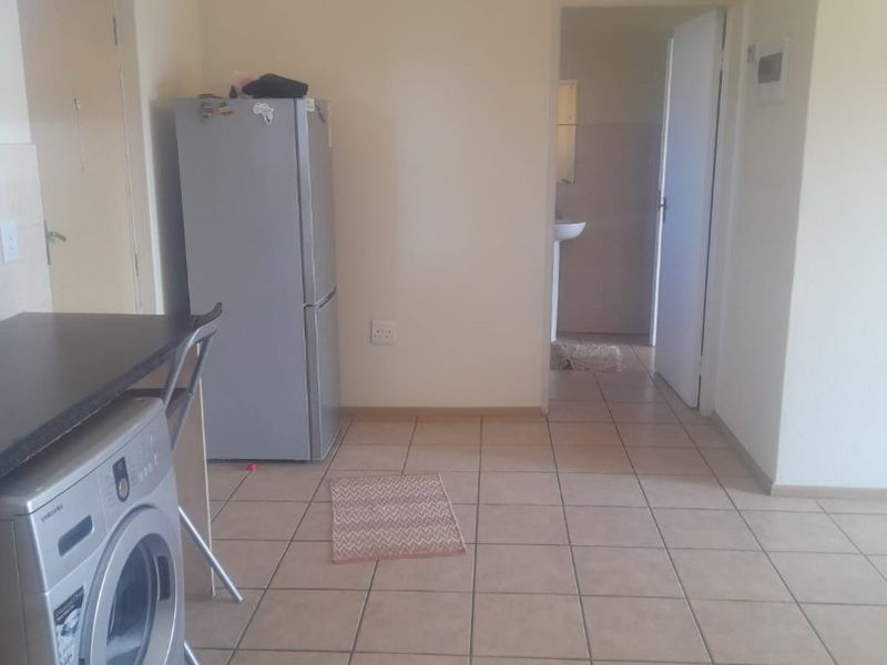 An open-plan living area featuring tiled flooring and a built-in kitchen counter, with direct access to an adjacent room.