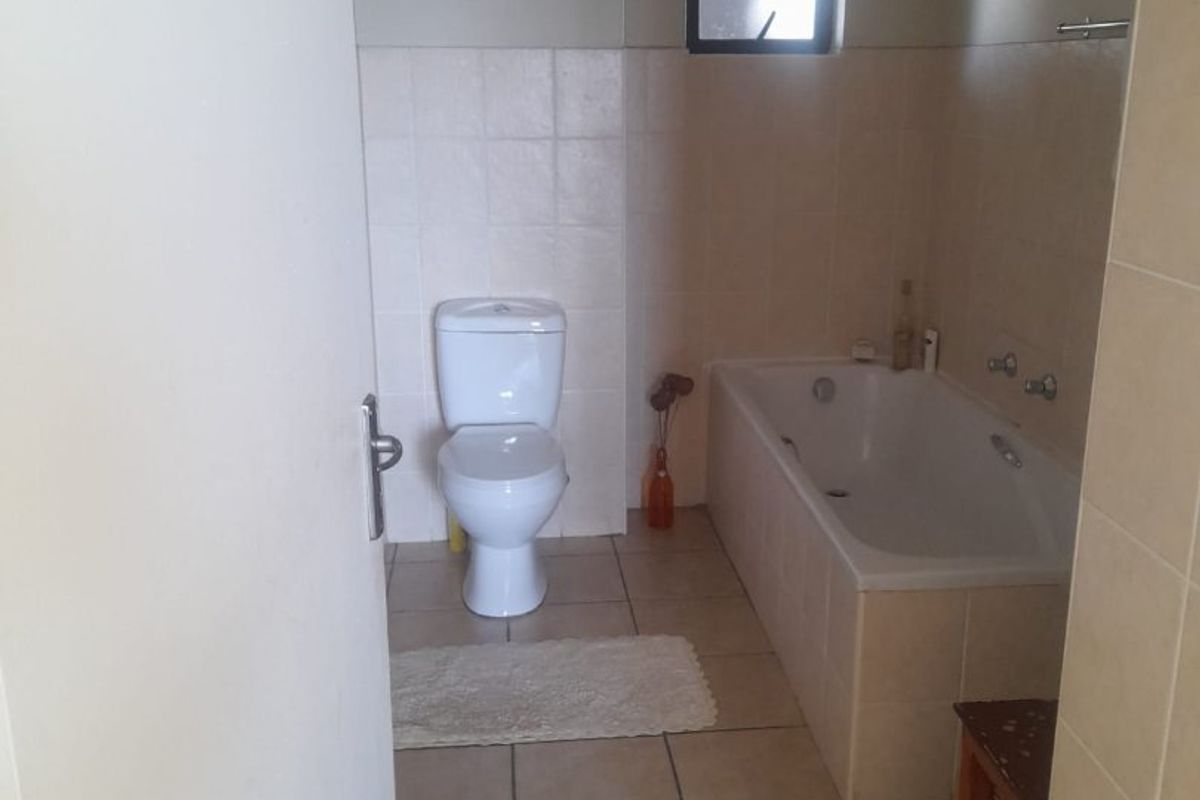A functional bathroom featuring a standard bathtub, toilet, and neutral tiled finishes throughout.