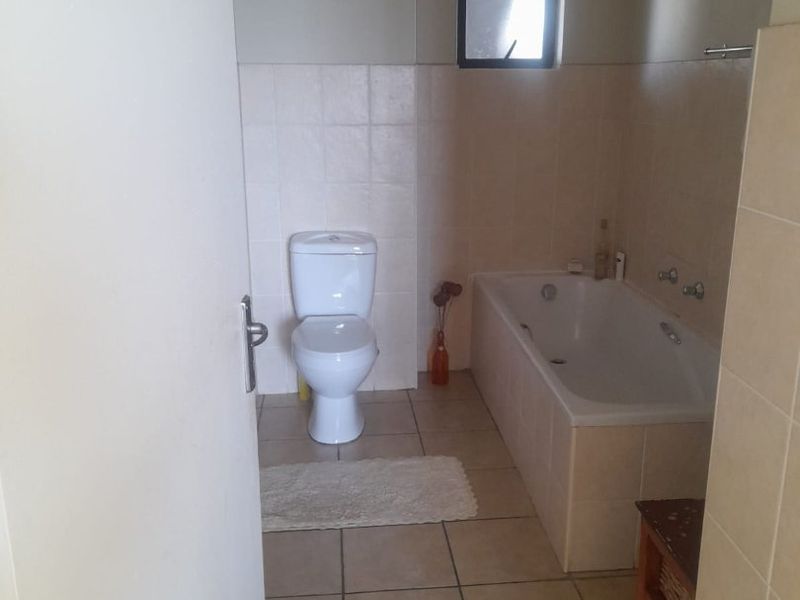 A functional bathroom featuring a standard bathtub, toilet, and neutral tiled finishes throughout.