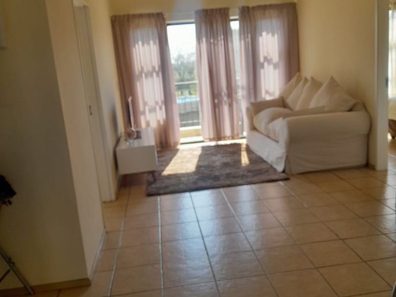 A living room featuring tiled flooring, clerestory windows, and a sliding glass door providing access to an outdoor area.