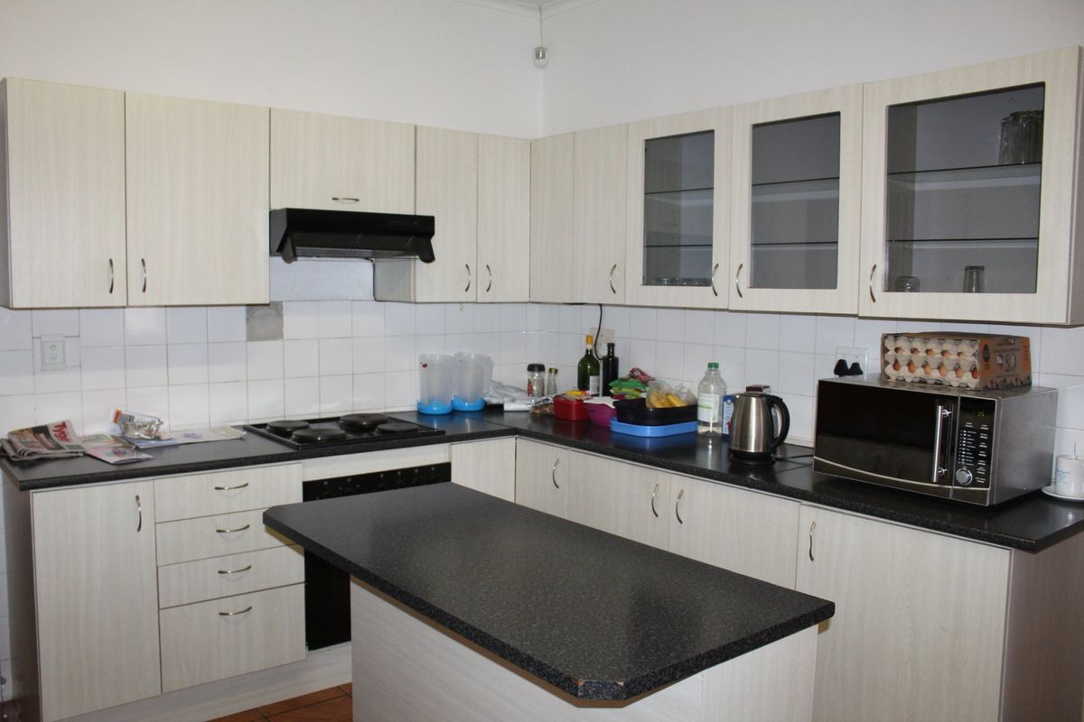 A functional kitchen featuring light-toned built-in cabinetry, dark laminate countertops, a central island, and a tiled backsplash with integrated cooking appliances.