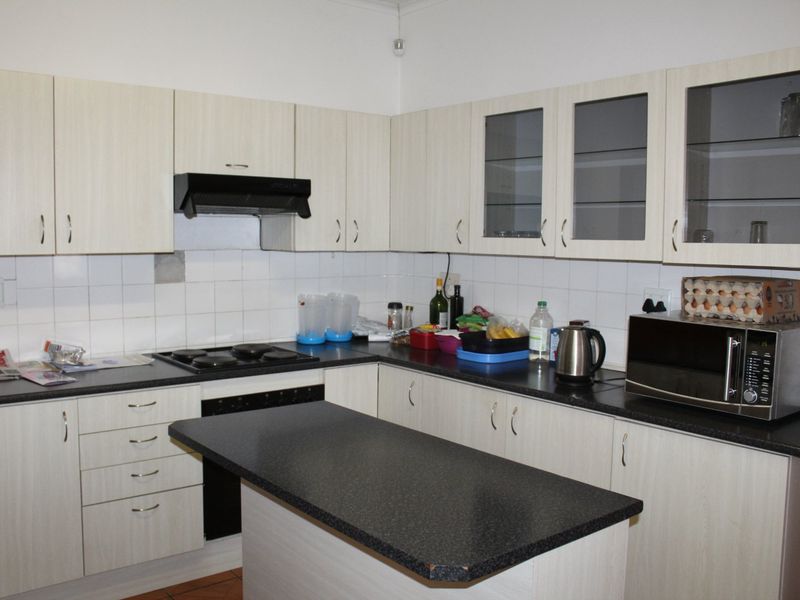 A functional kitchen featuring light-toned built-in cabinetry, dark laminate countertops, a central island, and a tiled backsplash with integrated cooking appliances.