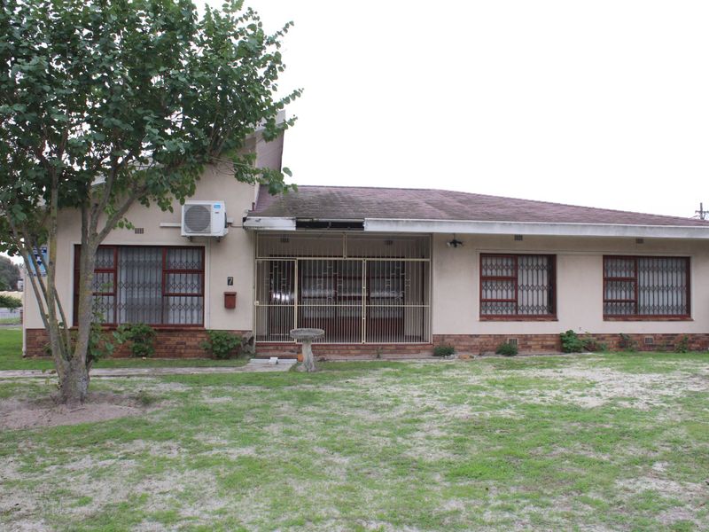 Front elevation of a single-story house featuring security gates, brick base detailing, and an external air conditioning unit, set on a large grassed plot.