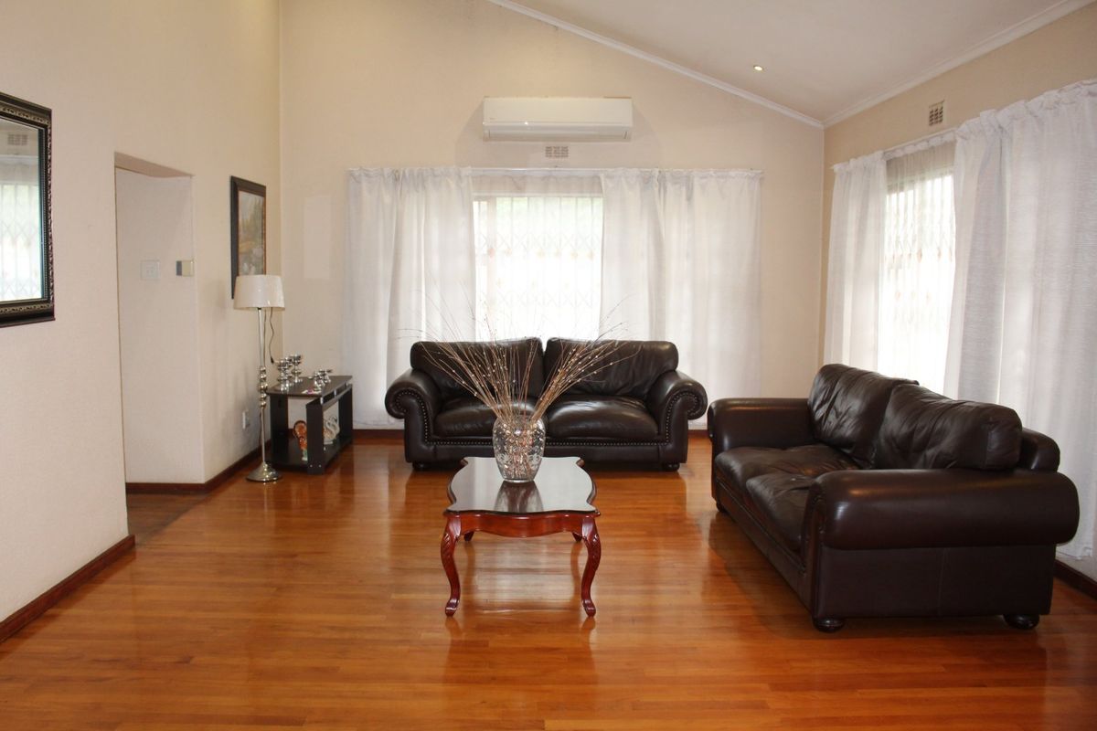 Spacious living room featuring polished hardwood flooring, a high vaulted ceiling, and a wall-mounted split-system air conditioning unit.