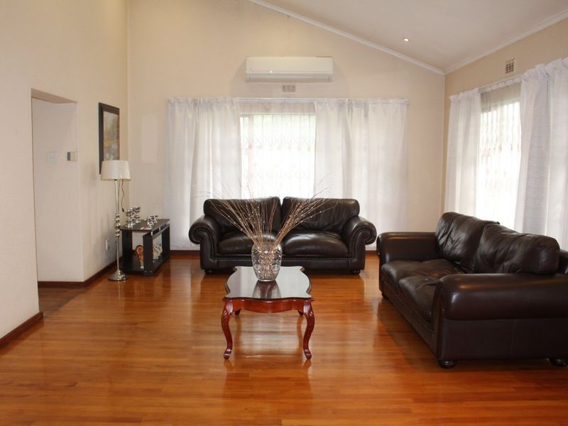 Spacious living room featuring polished hardwood flooring, a high vaulted ceiling, and a wall-mounted split-system air conditioning unit.