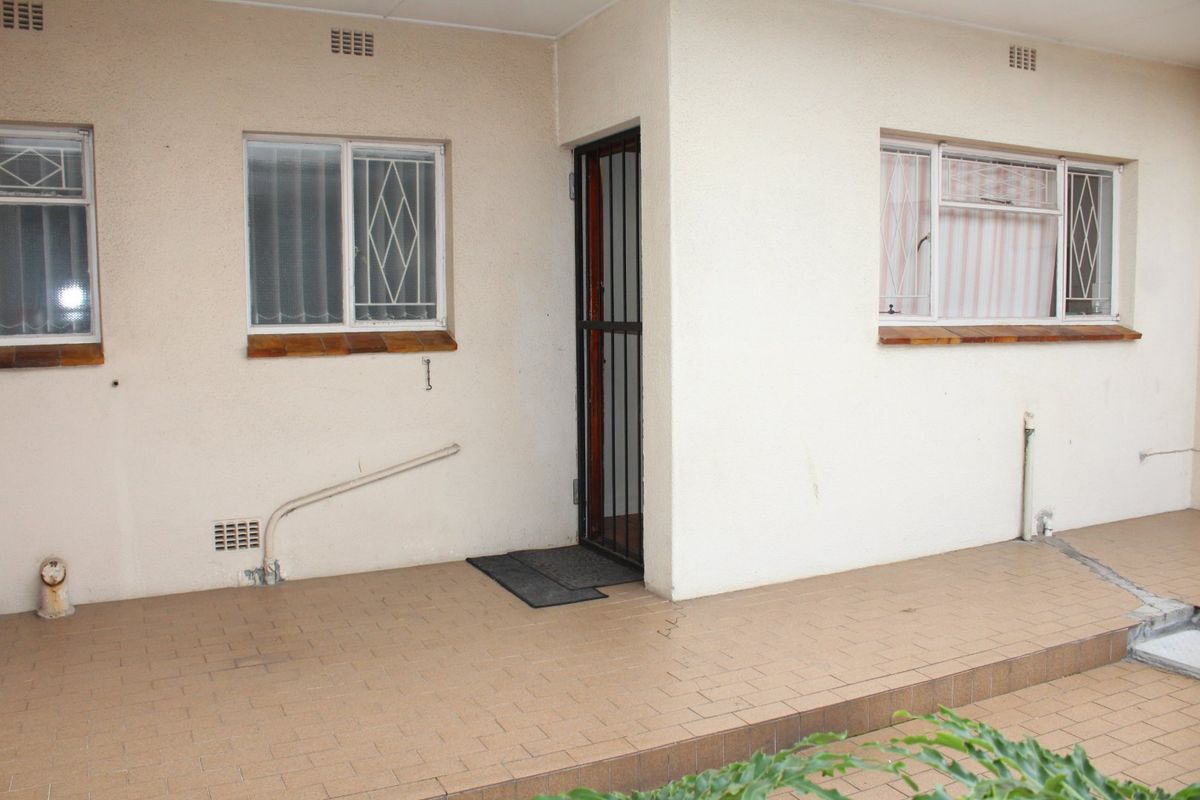 A paved rear patio area featuring security gates, sliding windows with security bars, and exterior brick sills.