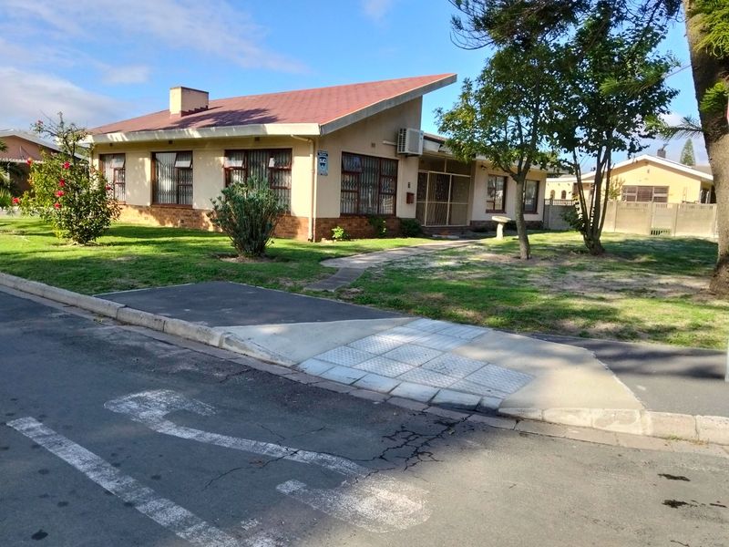 Front view of a single-story residential house featuring a pitched roof, brick exterior, and established garden with a paved walkway.