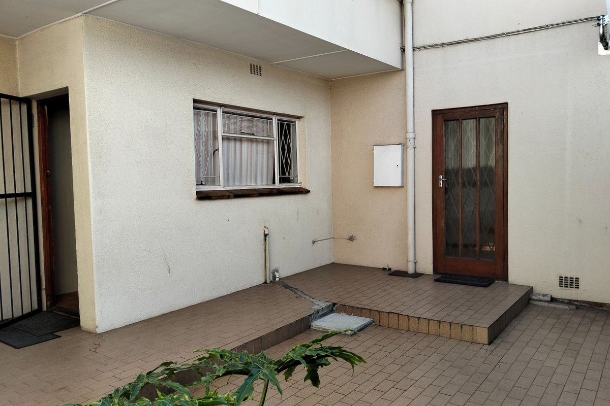 A rear patio area featuring tiled flooring, a timber-framed door, and security-fitted windows, requiring some maintenance to the flooring and exterior finishes.