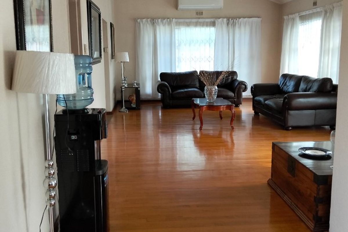 Spacious living room featuring polished hardwood flooring, a high vaulted ceiling, and a wall-mounted split-system air conditioning unit.