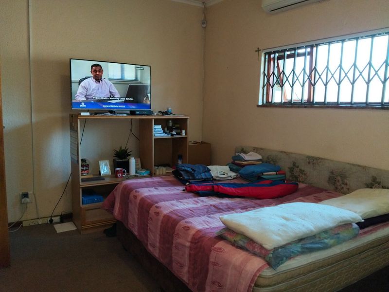 A functional bedroom featuring a window with security bars and a wall-mounted air conditioning unit.