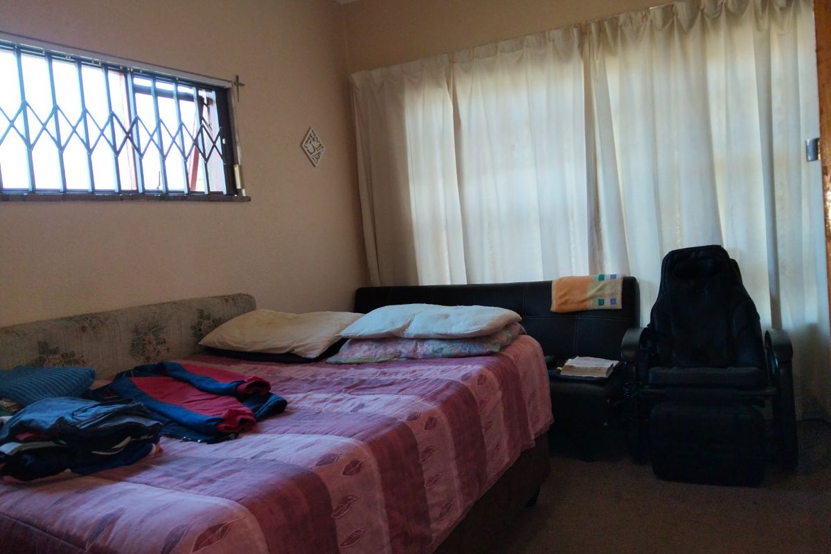 A functional bedroom featuring a window with a security gate and neutral wall finishes, offering a blank canvas for potential interior updates.