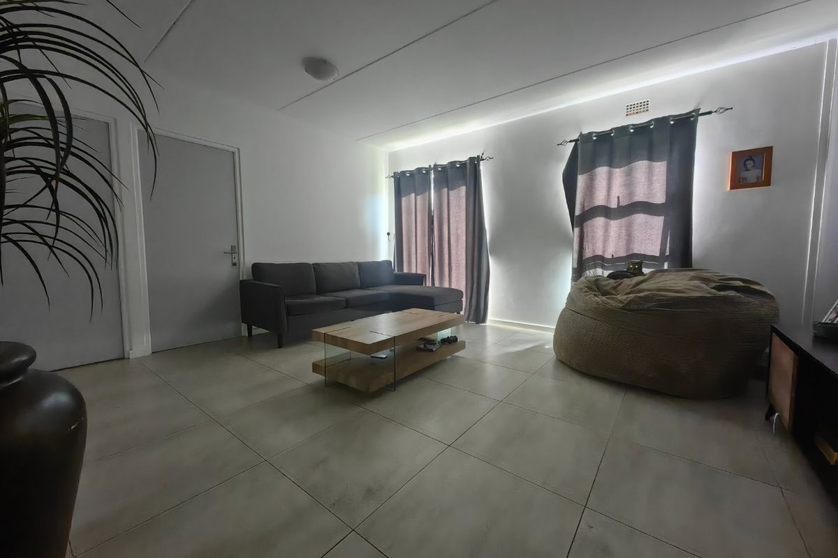 A spacious living room featuring large format floor tiles, neutral walls, and recessed ceiling lighting, providing a clean and functional living space.