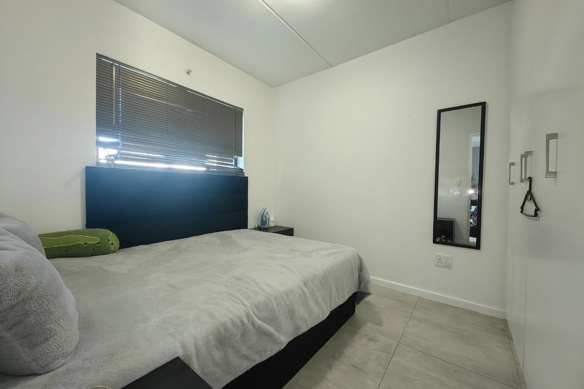 A clean and functional bedroom featuring tiled flooring, built-in cupboards, and venetian blinds, offering a neutral space ready for personalization.