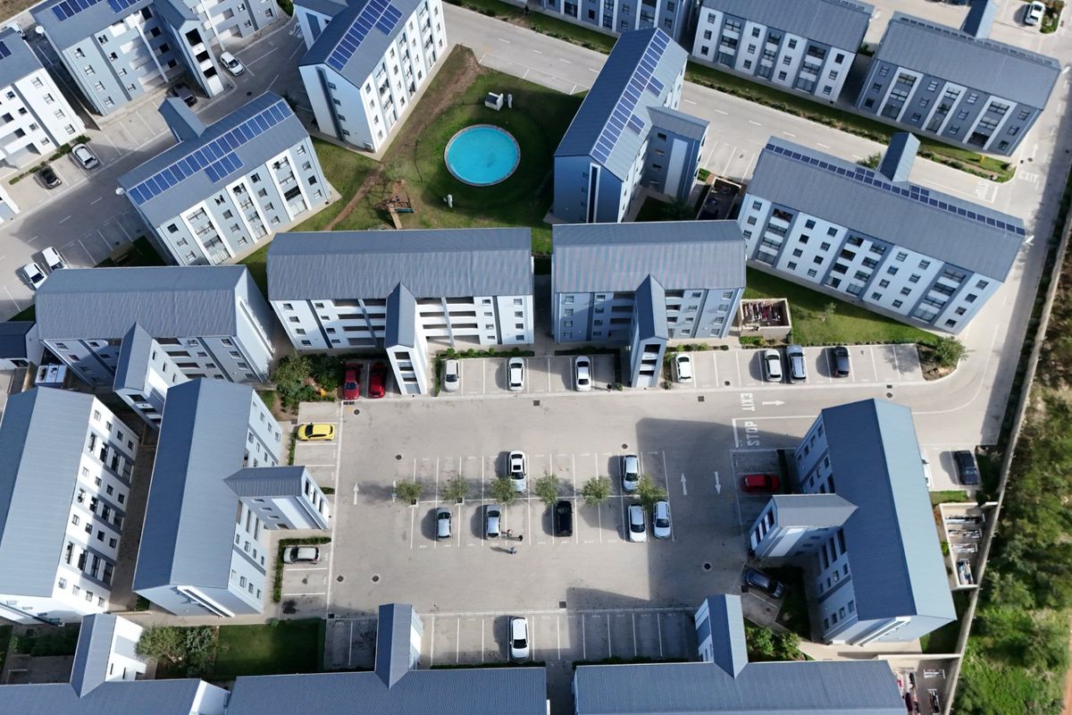 Aerial view of a modern apartment complex featuring multiple residential blocks, paved parking areas, and a communal swimming pool.