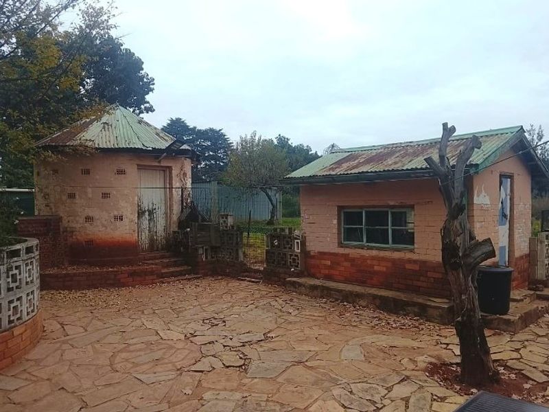 Rear courtyard area featuring two small outbuildings with corrugated metal roofs and stone paving, showing significant signs of weathering and wear.
