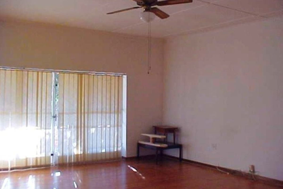 A spacious, empty living room featuring hardwood flooring, a ceiling fan, and large sliding glass doors with vertical blinds for natural light.