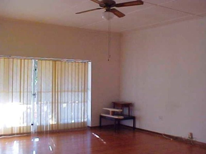 A spacious, empty living room featuring hardwood flooring, a ceiling fan, and large sliding glass doors with vertical blinds for natural light.
