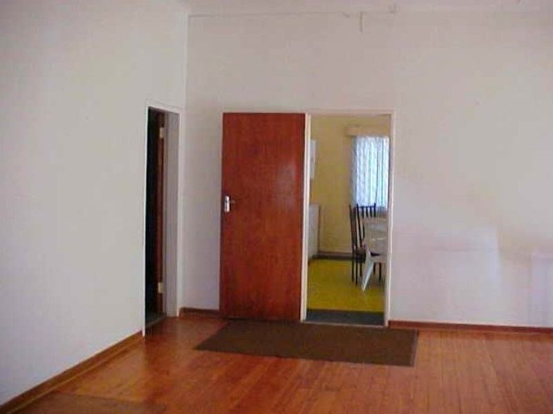 An empty living area featuring wooden flooring and internal wooden doors, leading into an adjacent room.