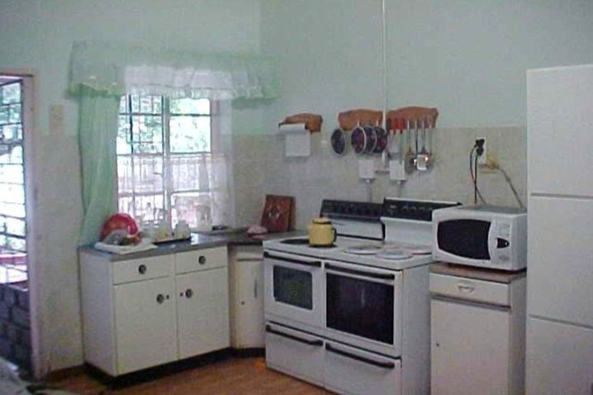 A dated kitchen featuring white cabinetry, a freestanding stove, and tiled splashbacks, offering potential for a modern renovation.