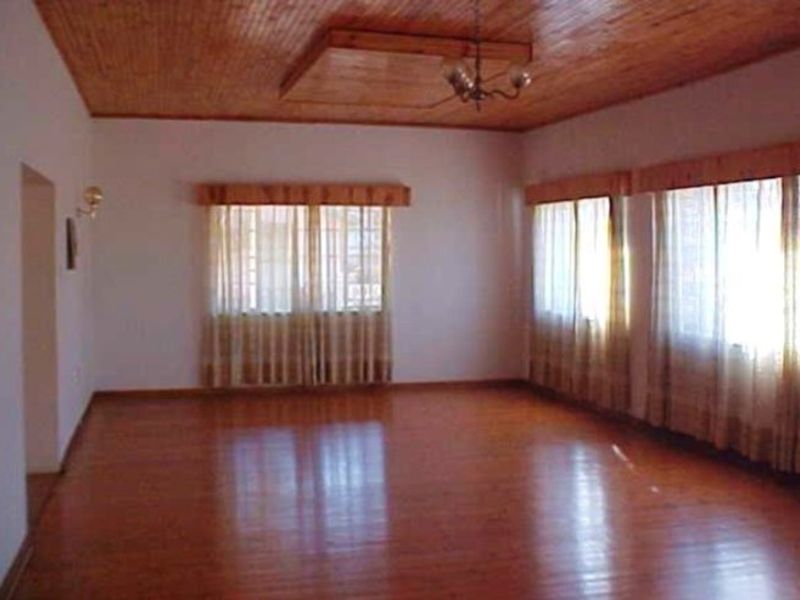 Spacious living room featuring polished hardwood flooring and a traditional timber-paneled ceiling with a central light fixture.