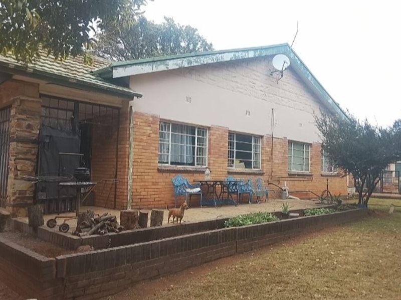 Rear view of a single-story brick house featuring a raised garden planter, tiled roof, and security gates on the patio area.