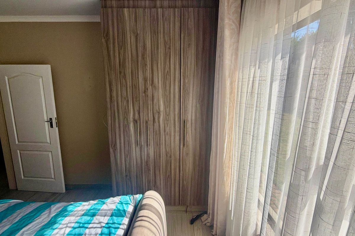 A bedroom featuring wood-grain built-in wardrobes, laminate flooring, and natural light through large windows.