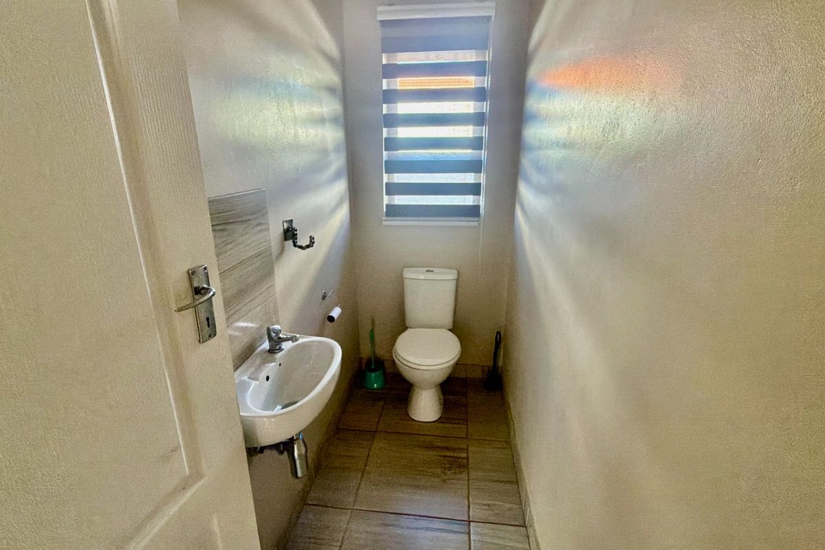 A compact, functional guest bathroom featuring a wall-mounted basin, toilet, and tiled flooring with a window for natural light.