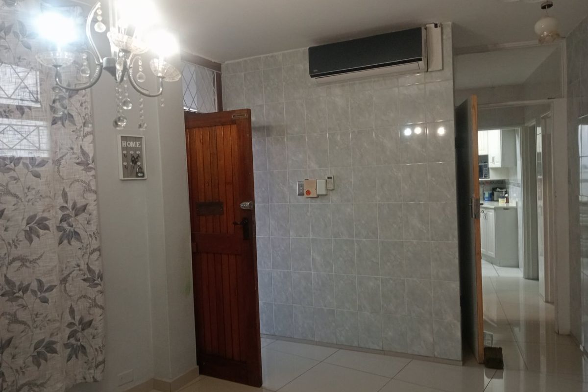 Living area featuring tiled flooring, a wall-mounted air conditioning unit, and a tiled feature wall, with a view through to the kitchen area.