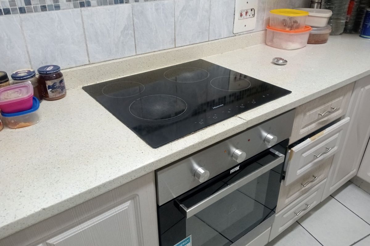 A functional kitchen area featuring a built-in oven, electric hob, stone countertops, and tiled backsplash with cabinetry.