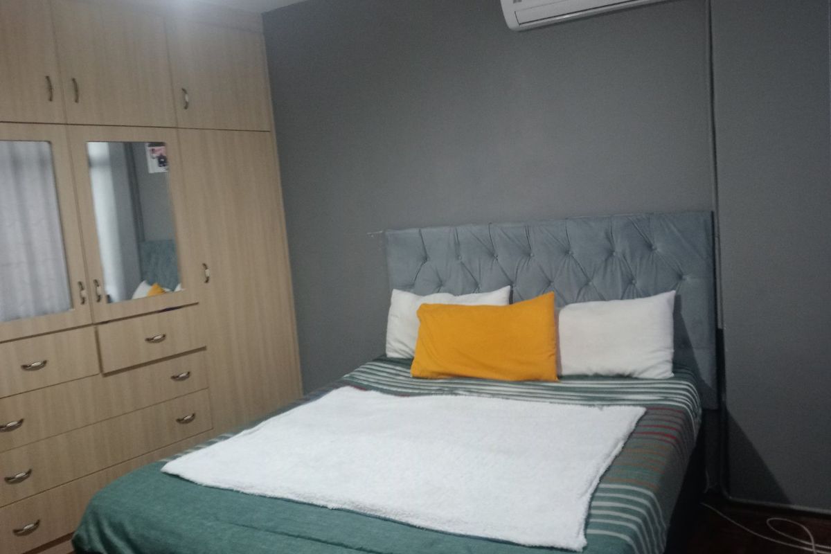 A well-maintained bedroom featuring a large built-in wardrobe with integrated mirror and a wall-mounted air conditioning unit.