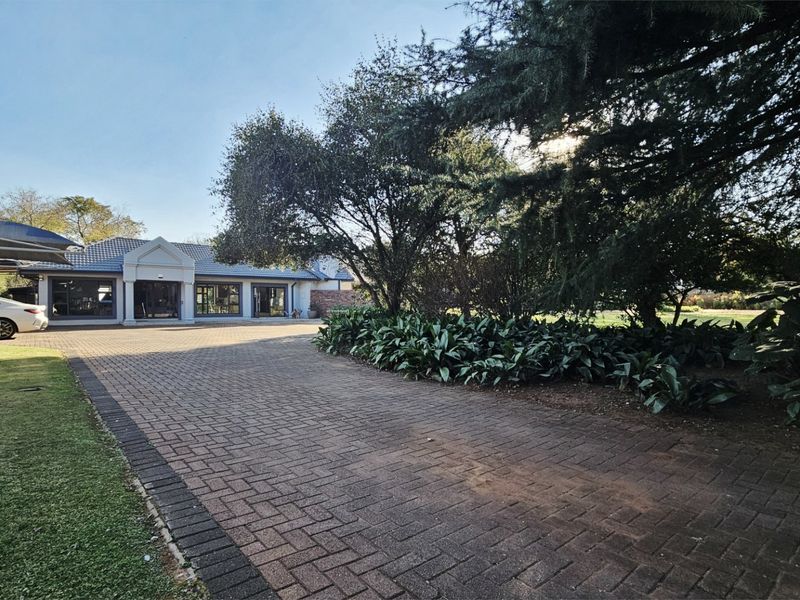 Spacious front exterior view featuring a paved driveway, established garden, and a covered carport area leading to the main house entrance.