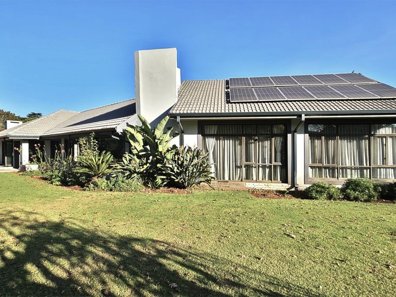 Rear view of the house featuring a tiled roof with solar panels, a prominent chimney, and large sliding glass doors opening onto a garden patio.
