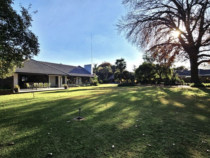 Spacious rear garden featuring a well-maintained lawn, mature trees, and a covered patio area attached to the main residence.