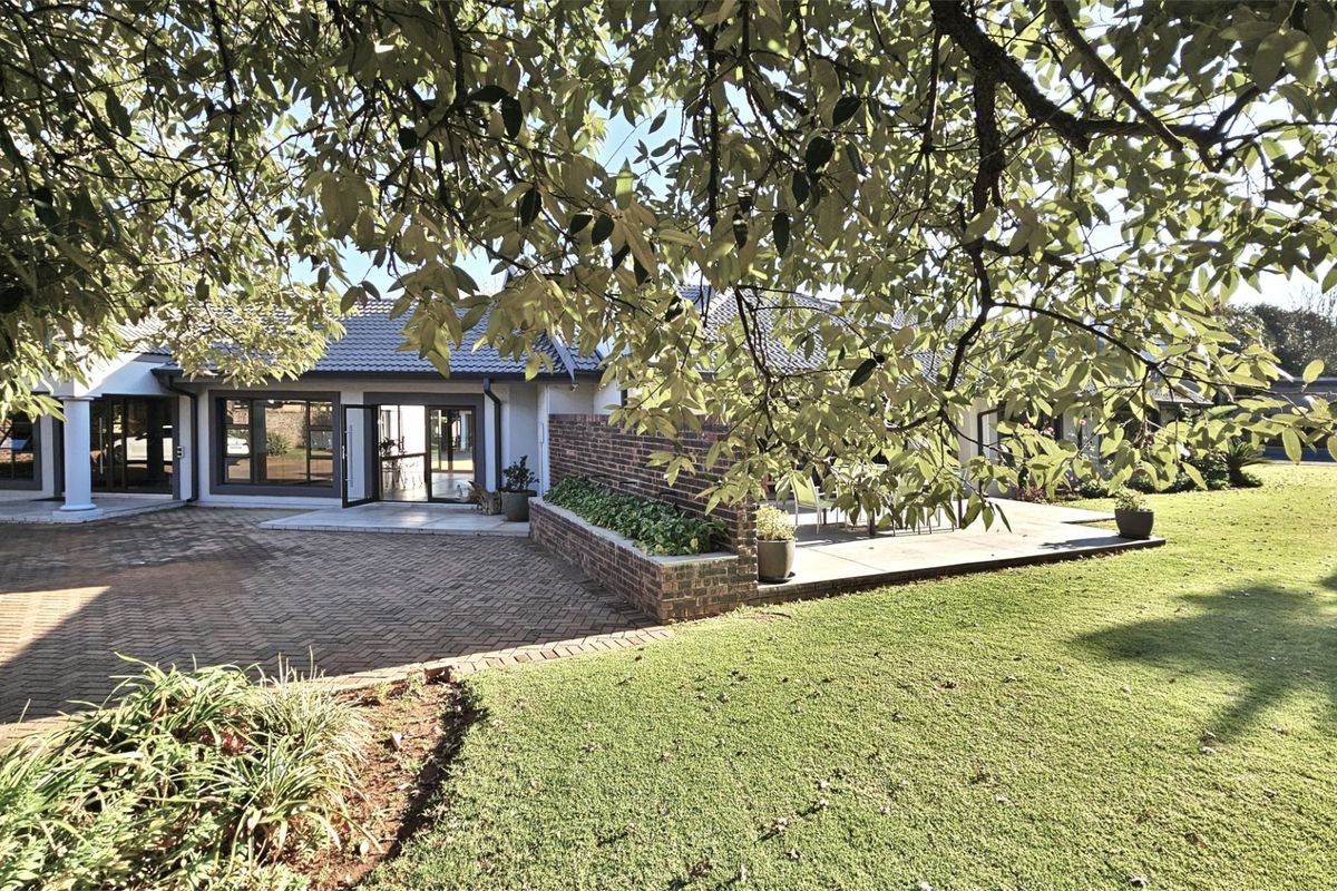 Rear view of the property featuring a paved driveway, raised brick planter, and a spacious patio area leading into the home.