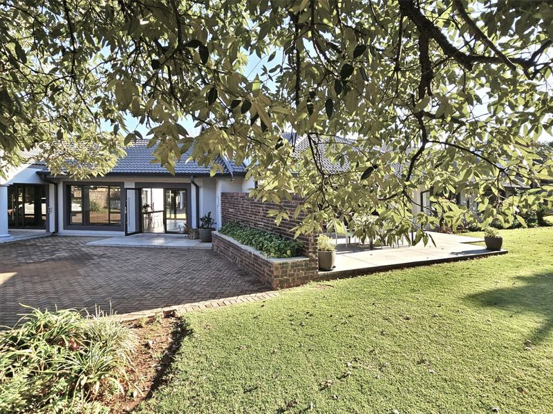 Rear view of the property featuring a paved driveway, raised brick planter, and a spacious patio area leading into the home.