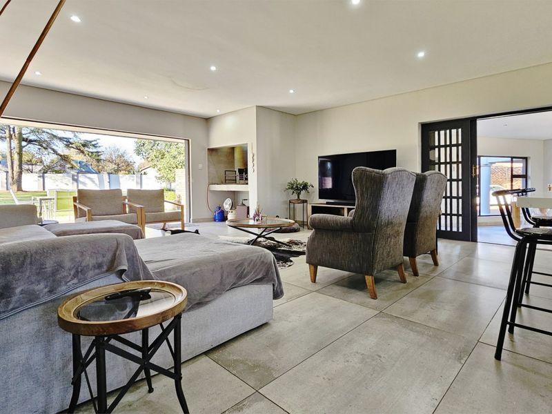 Spacious open-plan living area featuring large format floor tiles, recessed lighting, a built-in indoor braai, and seamless access to the outdoor space.