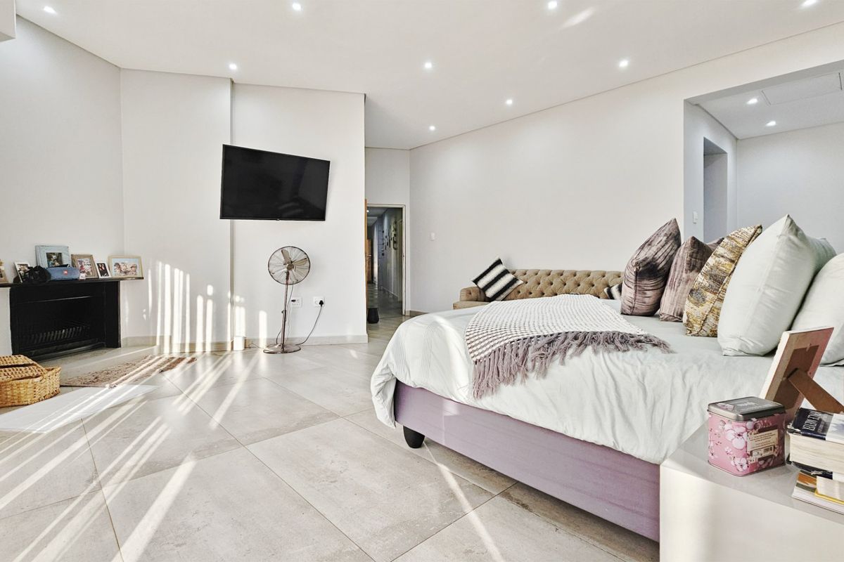Spacious bedroom featuring large format floor tiles, recessed downlighting, and a built-in fireplace, offering a bright and modern living environment.