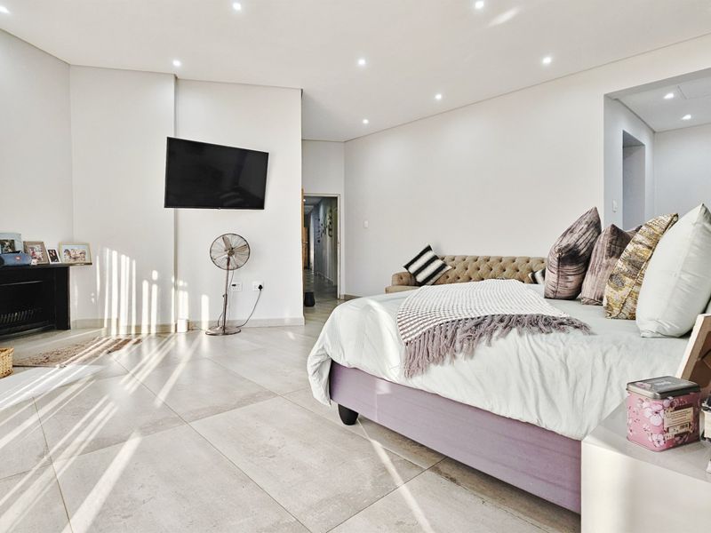 Spacious bedroom featuring large format floor tiles, recessed downlighting, and a built-in fireplace, offering a bright and modern living environment.
