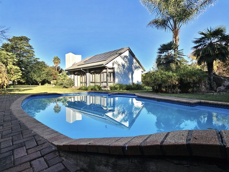 A well-maintained swimming pool area featuring brick paving, solar panels on the roof, and a landscaped garden setting.