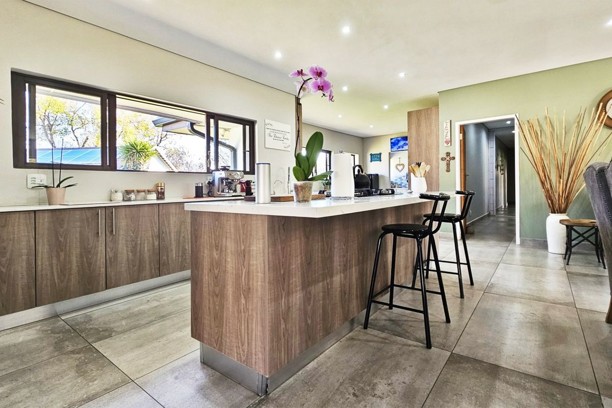 Modern kitchen featuring wood-finish cabinetry, a central island with stone countertops, and large windows providing natural light and garden views.