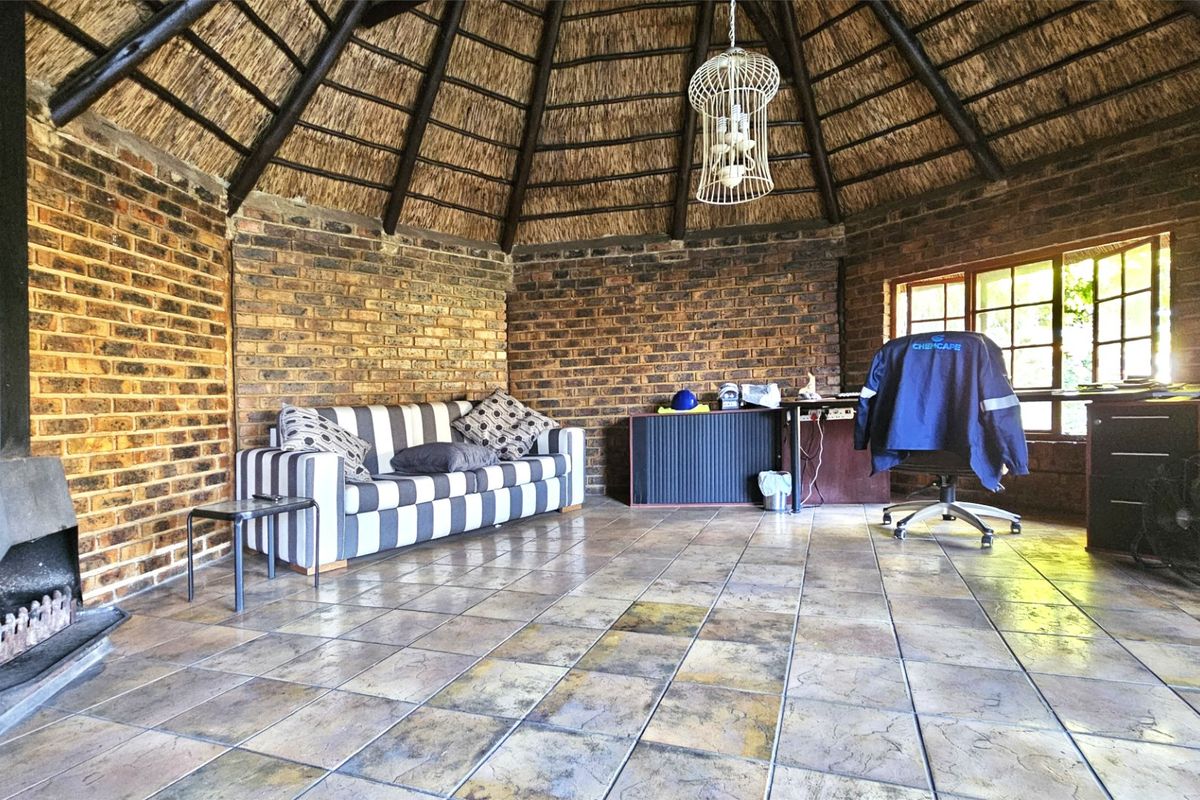 A rustic living area featuring a high thatched ceiling, exposed brick walls, tiled flooring, and a built-in fireplace.
